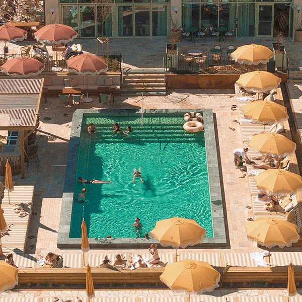 Utomhuspool på Hjortviken, parasoller och gäster som badar och kopplar av i naturnära miljö.